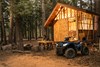 Front three-quarter view of an ATV parked in front of a cabin.