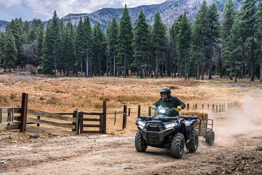 Front view of a person riding an ATV off-road towing a trailer. opens in a new window