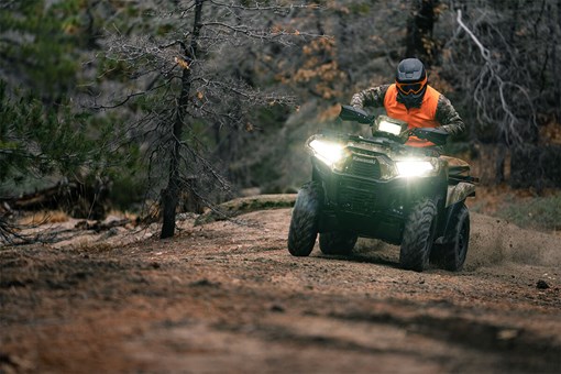 Front view of a person riding an ATV off-road with headlights on. opens in a new window