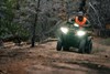 Front view of a person riding an ATV off-road with headlights on. 