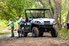 Three-quarter front angle of a parked side x side and two people fishing.