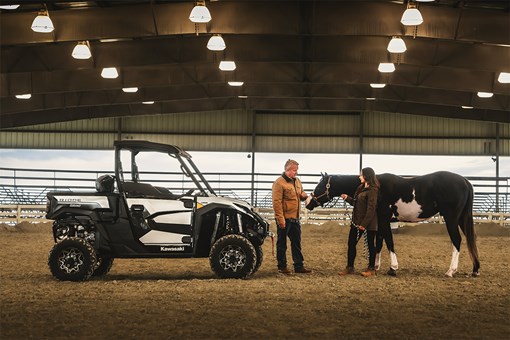 Side view of a side x side in a covered arena next to a horse. opens in a new window