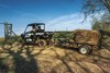 Front three-quarter angle of a person driving a side x side towing a trailer loaded with hay.