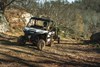 Front three-quarter angle of a person driving a side x side towing a trailer on a dirt road. 