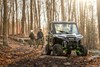 Front three-quarter view of a side x side parked in the woods with hikers.