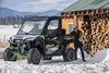 Front three-quarter view of a side x side parked in the snow next to a person.