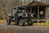 Rear three-quarter view of a side x side parked next to a cabin. 