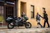 Side angle of a parked motorcycle with people in the background walking.