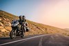 Three-quarter front angle of a person and a passenger riding a motorcycle on a highway.