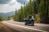 Three-quarter front angle of a person riding a motorcycle on a highway with trees in the background.