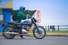 Side angle of a person standing near a blue motorcycle.