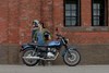 Side angle of two people standing near a parked motorcycle.