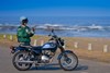 Side angle of a person standing near a parked motorcycle.