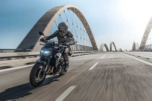 Three-quarter front angle of a person riding a motorcycle on a bridge. opens in a new window