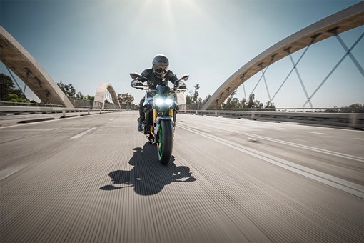 Front angle of a person riding a motorcycle on a bridge. opens in a new window
