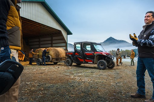 Side view of a side x side towing a trailer hauling hay backing into a barn. opens in a new window