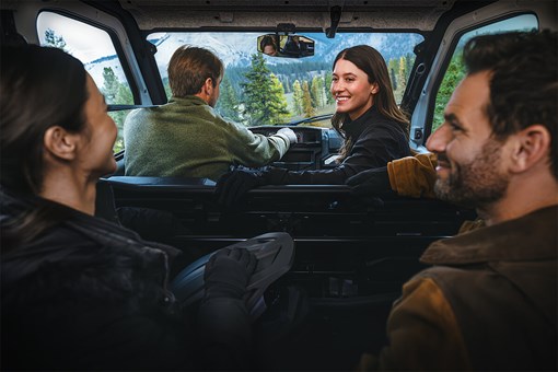 Interior of a parked side x side with enclosed cab and four adults chatting. opens in a new window