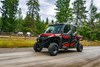 Three-quarter front angle of a side x side driving down a dirt road in front of a pasture.