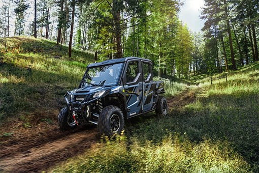 Front three-quarter view of a side x side being driven on a road in the woods. opens in a new window