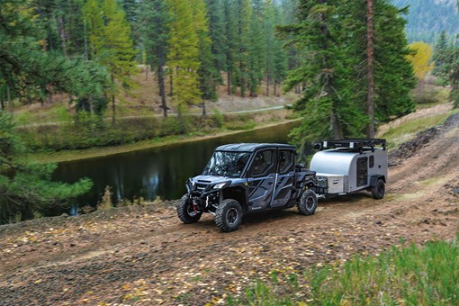 Side x side towing a small camper trailer down a dirt road. opens in a new window
