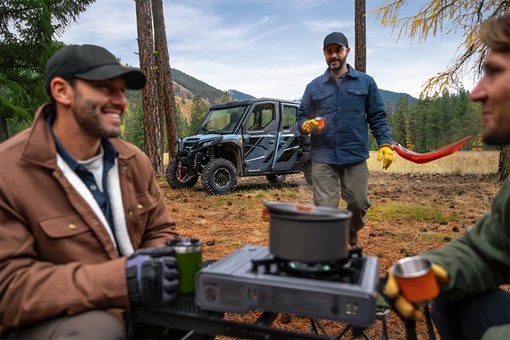 Men having coffee in a campground with a side x side in the background. opens in a new window