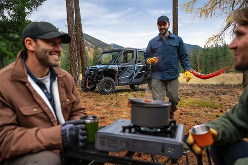 Men having coffee in a campground with a side x side in the background. opens in a new window
