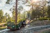 Rear view of two side x sides towing utility trailers up a dirt road through the trees. 