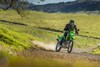 Front angle of a person riding a motorcycle on a dirt road across a green meadow.