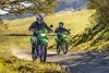 Front angle of two people riding green dual-sport motorcycles down a dirt road.