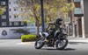 Front three-quarter view of a person riding a motorcycle around a city corner.