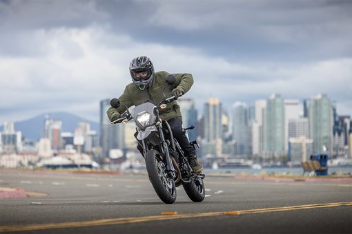 Front view of a person riding a motorcycle against a cityscape background. opens in a new window