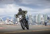 Front view of a person riding a motorcycle against a cityscape background.