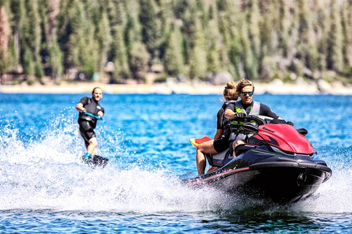 Front angle of two people riding a personal watercraft towing a wakeboarder. opens in a new window