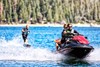 Front angle of two people riding a personal watercraft towing a wakeboarder.