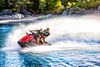 Front angle of two people riding a personal watercraft on the water.