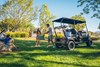 Three-quarter rear angle of a Neighborhood Activity Vehicle parked on grass with a family nearby.