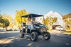 Three-quarter front angle of two people riding in a Neighborhood Activity Vehicle on a community roadway.