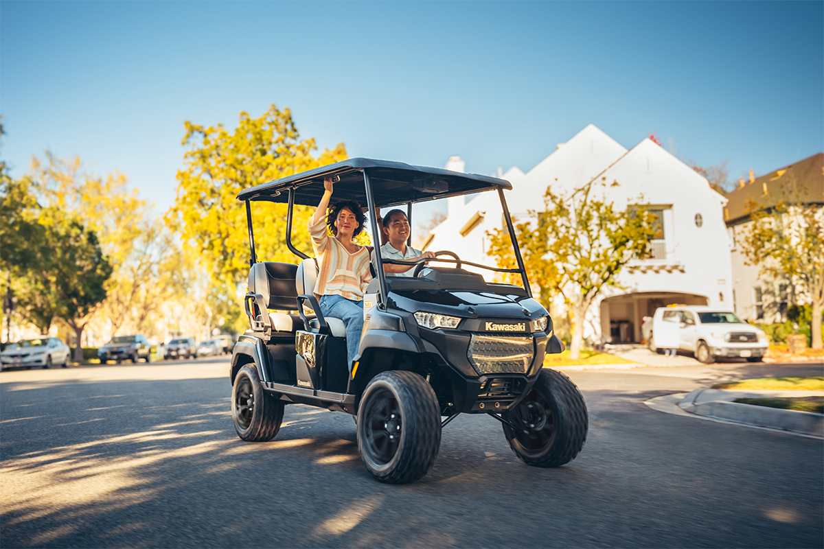 Three-quarter front angle of two people riding in a Neighborhood Activity Vehicle on a community roadway.