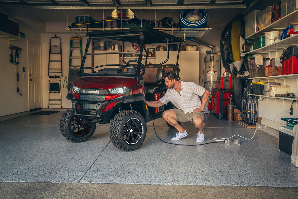 Three-quarter front angle of a person charging a Neighborhood Activity Vehicle inside a garage.