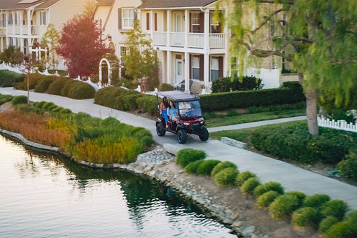 Three-quarter front angle of a family riding in a Neighborhood Activity Vehicle past a pond. opens in a new window