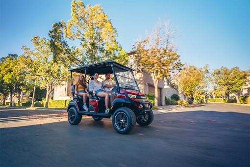 Three-quarter front angle of a family riding in a red Neighborhood Activity Vehicle on a community roadway. opens in a new window