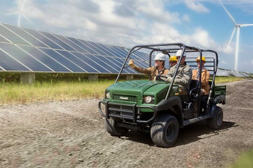 Three-quarter front angle of four people riding a side x side on a jobsite. opens in a new window