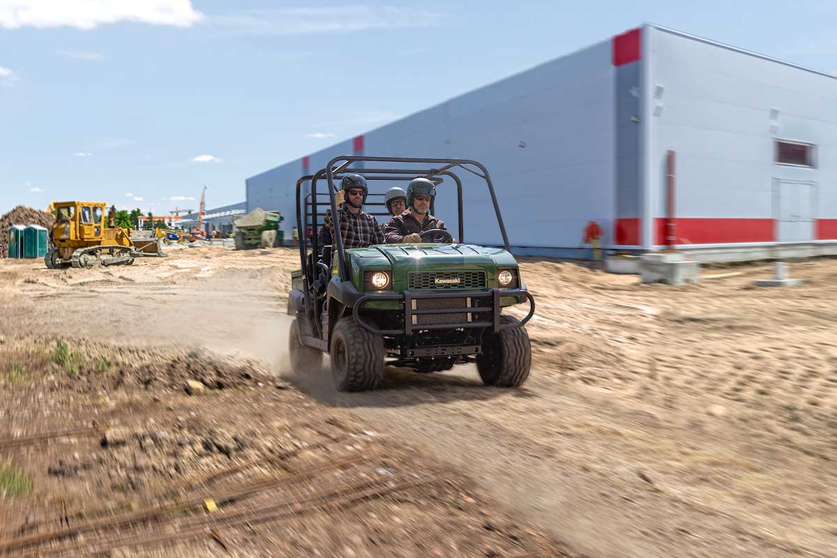Front angle of three people riding a side x side on a jobsite.