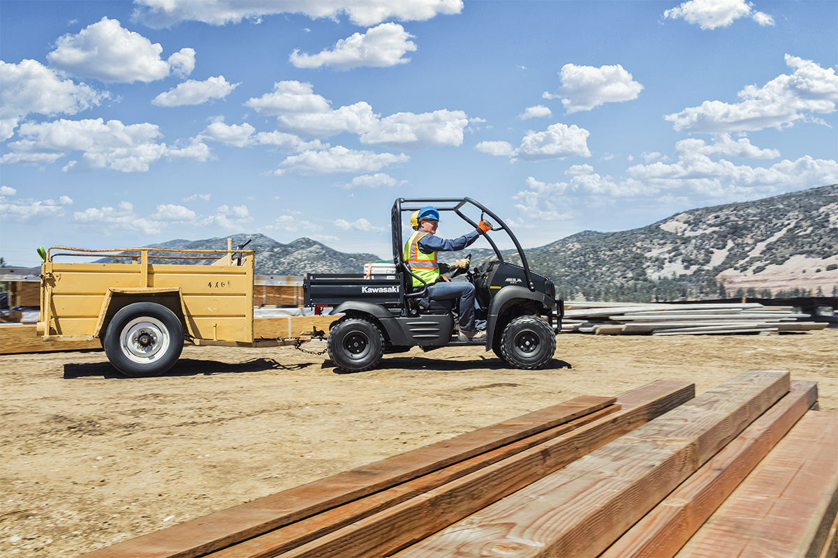 Side angle of two people driving a side x side at a jobsite.
