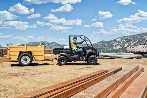 Side angle of two people driving a side x side at a jobsite. opens in a new window