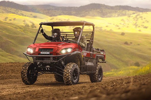 Three-quarter front angle of two people driving a red side x side off-road. opens in a new window