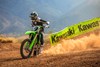 Three-quarter front angle of a person riding a green motorcycle on a dirt track.