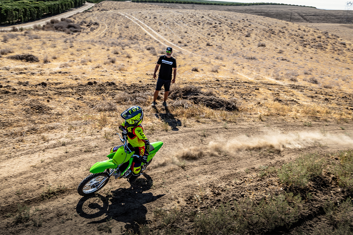 Aerial angle of a person riding a motorcycle off-road under adult supervision.
