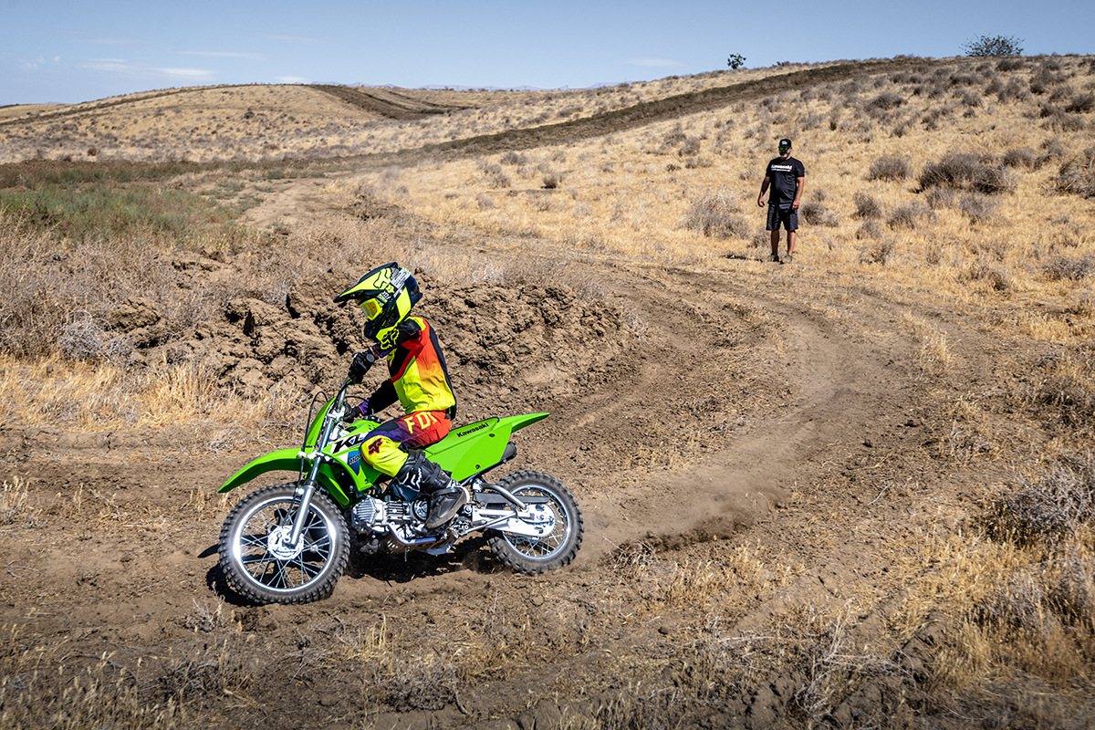 Profile angle of a person riding a motorcycle off-road under adult supervision.