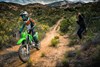 Front angle of a person riding a green motorcycle off-road under adult supervision.